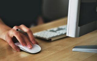 Free A hand using a wireless mouse at a modern desk setup with a computer and keyboard. Stock Photo